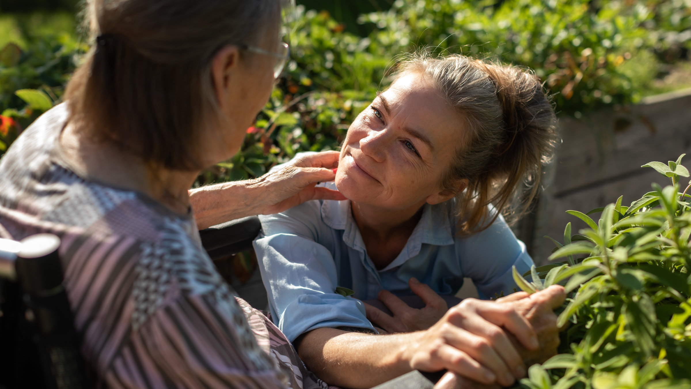 "Mitgefühl - Pflege neu denken": Alte gebrechliche Frau wird von blonder Pflegerin liebevoll gehalten.