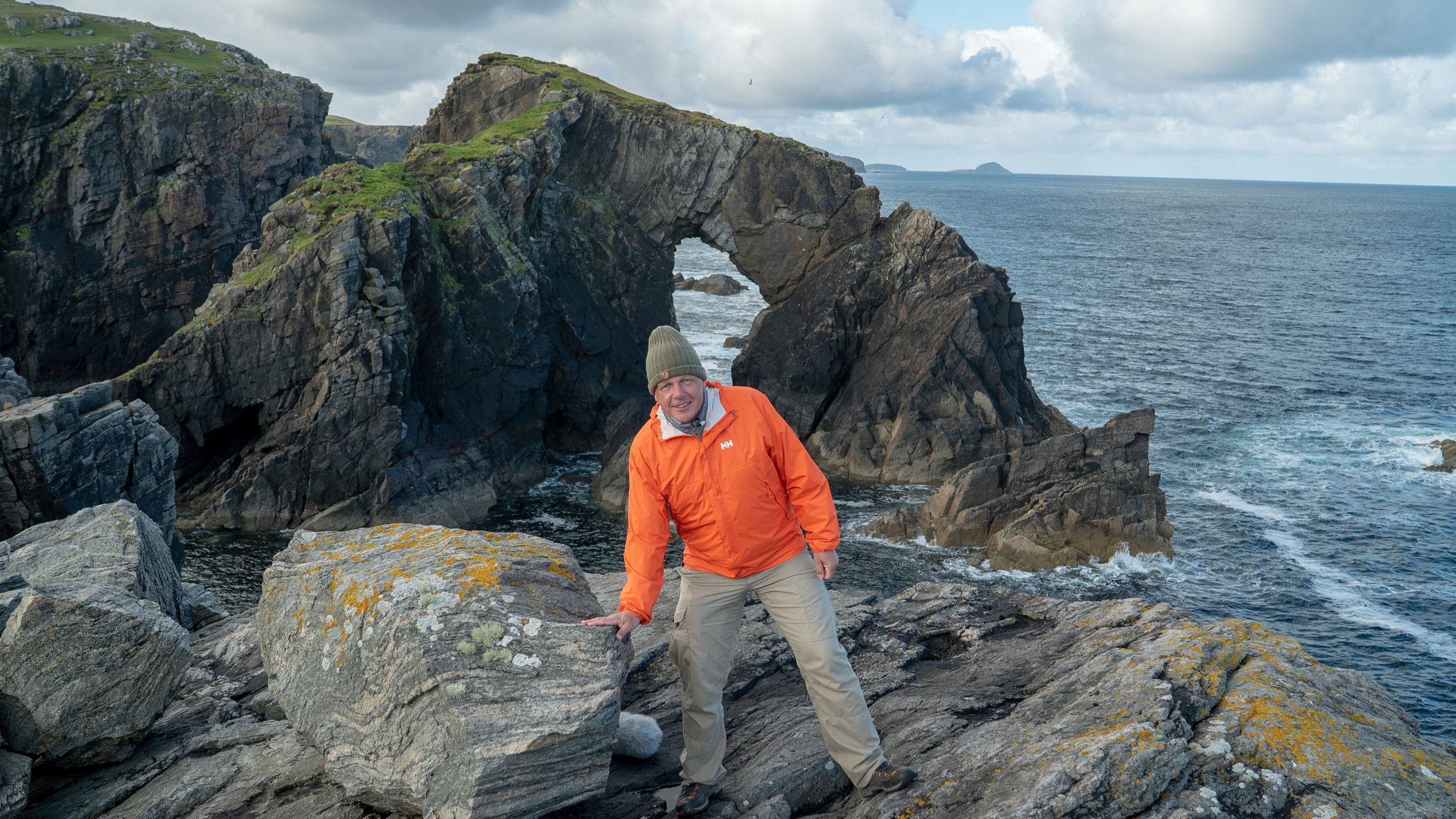 "Terra X: Expedition Europa: Die Geburt des Kontinents": Colin Devey steht an der Steilküste der Insel Lewis neben einem Felsbrocken, auf den er seine Hand gelegt hat.