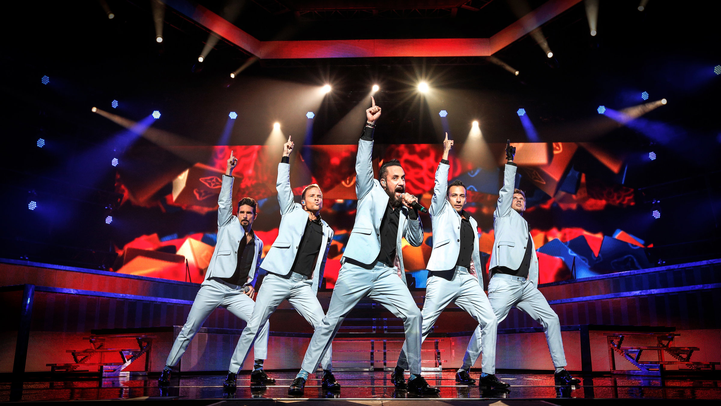 "Back Street Boys: In a World Like This - Live in Saitama": Die Bandmitglieder tanzend auf der Bühne. Alle strecken den linken Arm in die Höhe und machen einen großen Schritt zur Seite. Alle tragen hellblaue Anzüge und ein schwarzes Hemd.