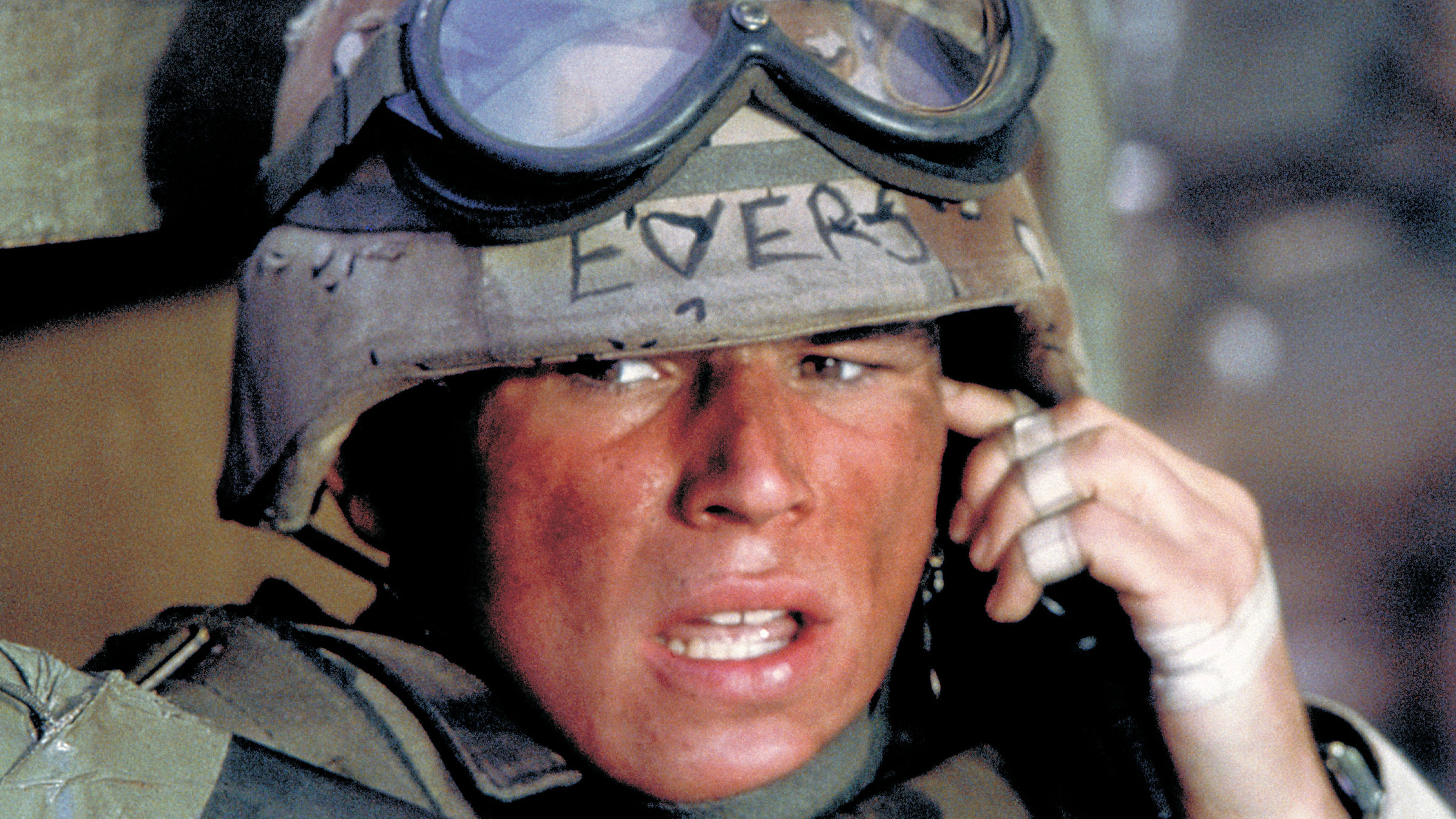 „Black Hawk Down“: Großaufnahme - Sergeant Eversmann (Josh Hartnett) in voller Kampfuniform mit Helm und hochgezogener Schutzbrille spricht angespannt in ein Gerät in seiner linken Hand, während er die Umgebung beobachtet.