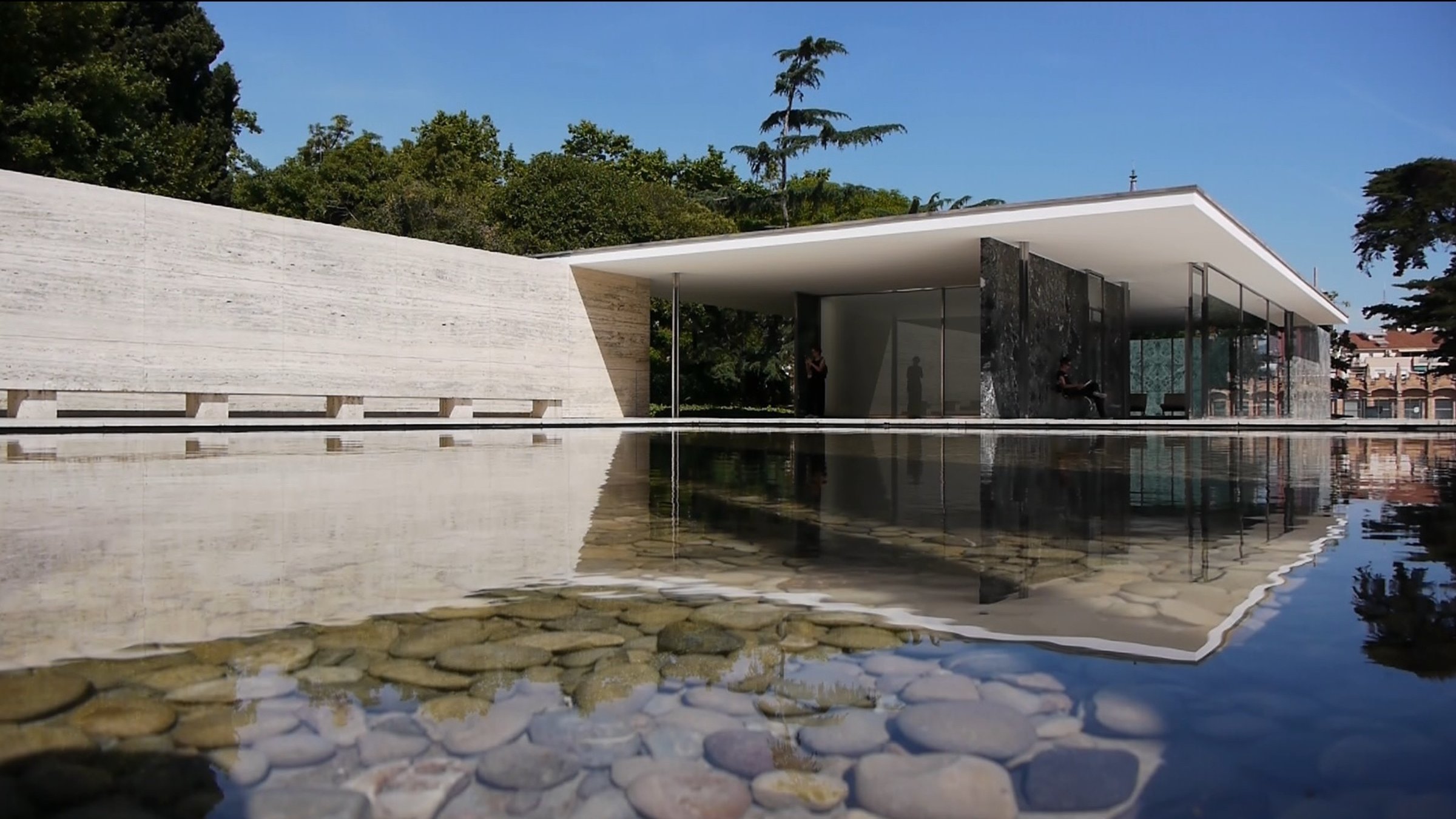 "Die Bauhaus-Revolution: Eleganter Flachdach-Bungalow, verglast, an einem Teich, im Wasser runde Steine. Dahinter Bäume.