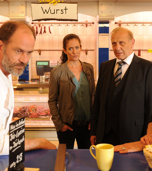 "SOKO Stuttgart - King of Vegan": Selma Kirsch (Yve Burbach) und Michael Kaiser (Karl Kranzkowski) stehen im Verkaufsraum der Metzgerei und reden mit Helena Meister (Karin Giegerich) und Willem Berg (Holger Daemgen), die nebeneinander an einem Stehtisch stehen.