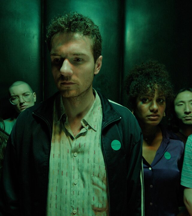 "This Is Gonna Be Great - Kontakt": Hanna (Mona Vojacek Koper), David (Rein Mulder), Aisha (Abigail Abraham) und Rob (Jonas Strand Gravli) stehen mit weiteren Personen (Komparsen) in einem grün beleuchteten Raum.