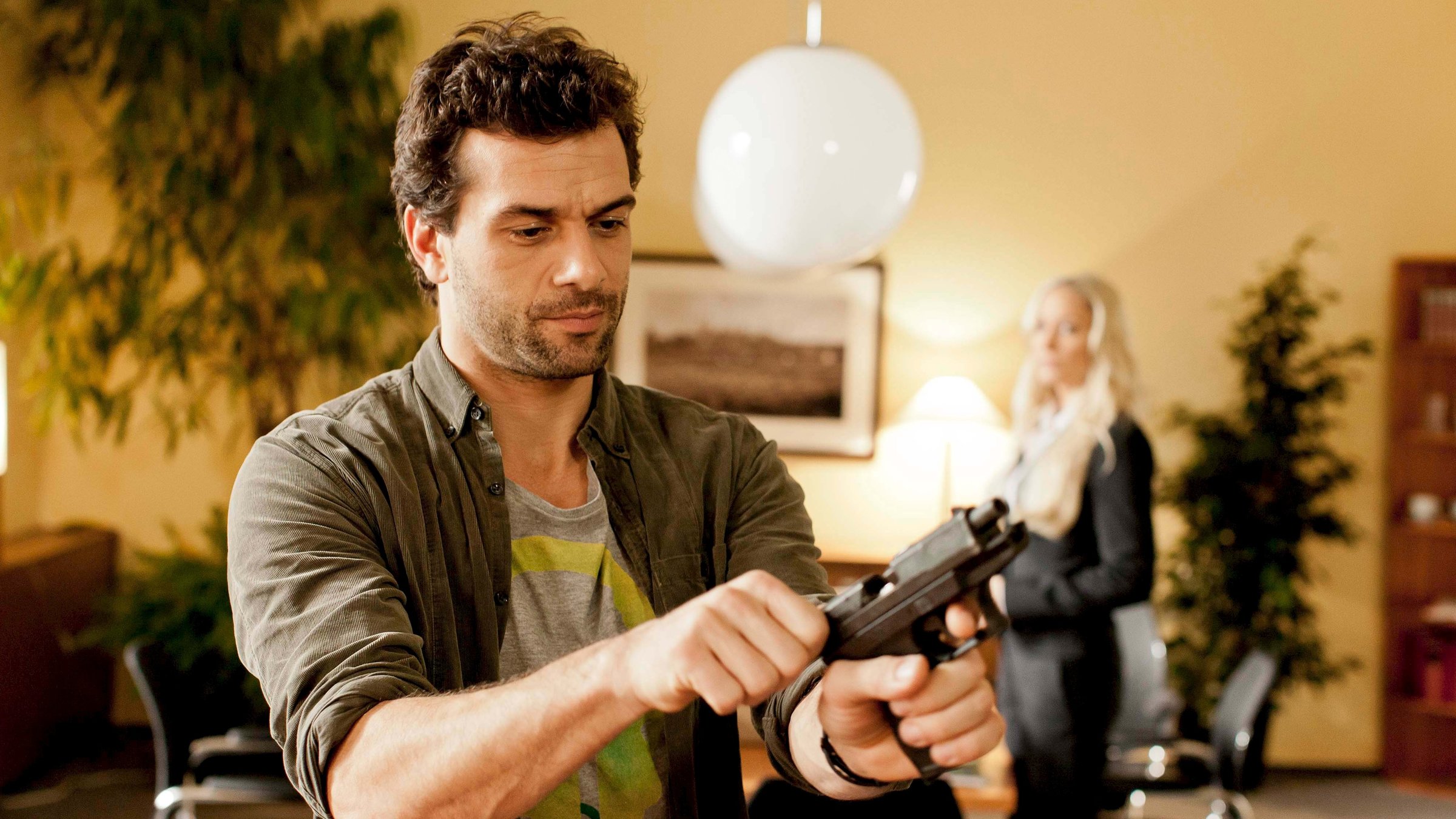 "Heldt - Explosive Fracht": Kommissar Heldt (Kai Schumann) und Staatsanwältin Ellen Bannenberg (Janine Kunze) in einem Büroraum. Heldt - im Vordergrund -  überprüft seine Pistole, Bannenberg sieht ihm dabei zu.