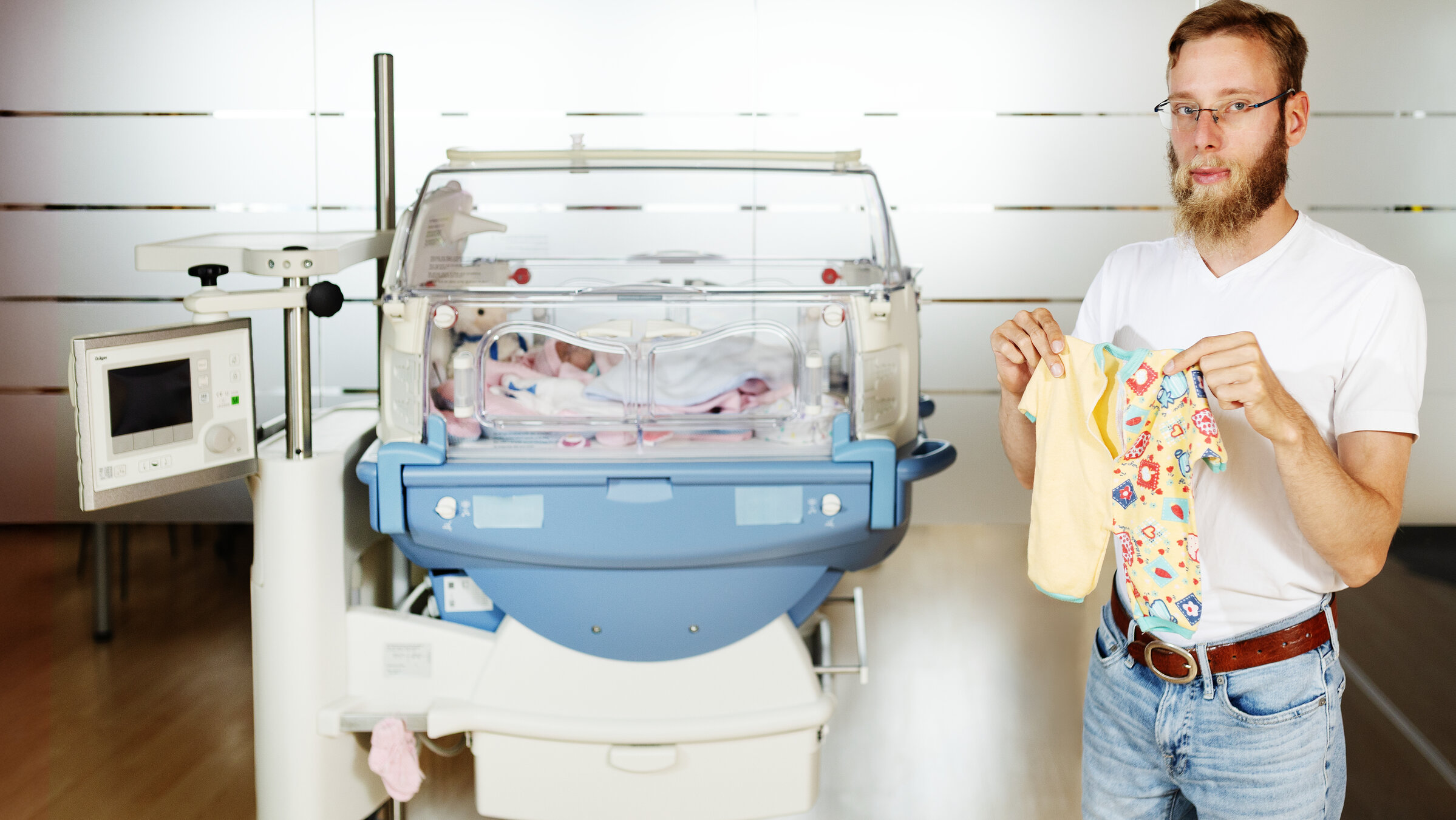 "37°Leben: Ich bin ein Frühchen": Lukas Mader (28) steht neben einem Brutkasten und hält seinen Strampler hoch.