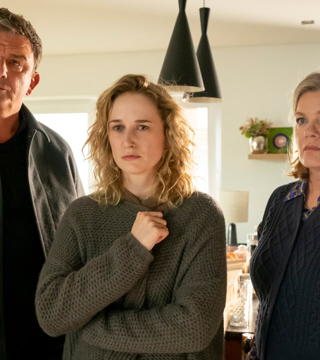 "Der Bergdoktor: Sternenkinder (2)": In der Küche der Familie Weiss: Ängstlich hält Jana Weiss (Pia Barucki) ihre Strickjacke fest vor der Brust zusammen und wirkt abwesend. Neben ihr stehen Dr. Martin Gruber (Hans Sigl) und Ulla Hoppe (Birge Schade). Beide blicken ernst.