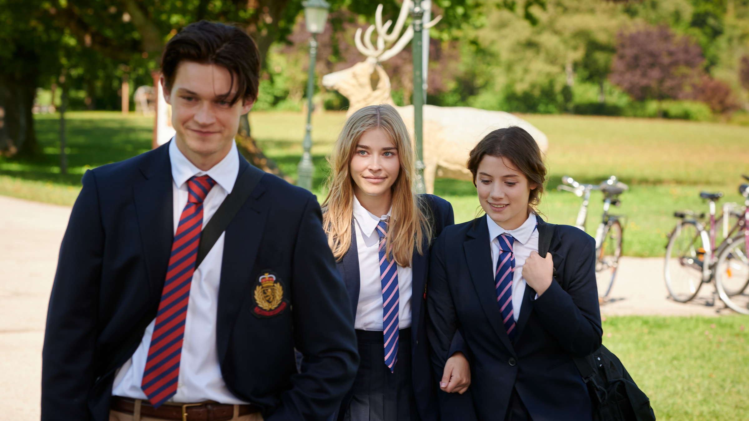 "Gestern waren wir noch Kinder (2)": Luisa (Milena Tscharntke) und Anna (Rieke Seja) laufen eingehakt hinter Peter (Damian Hardung) her. Luisas Blick ist auf Peter gerichtet. Alle lächeln.