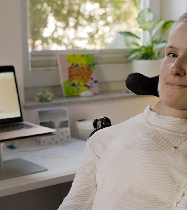 "einfach Mensch: Sina Wolf: Mein Engagement ist mir wichtig!": Sina Wolf sitzt vor einem Schreibtisch mit einem Laptop.