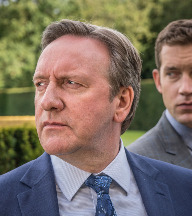 "Inspector Barnaby - Eine Hochzeit und dreieinhalb Todesfälle": DCI John Barnaby (Neil Dudgeon) und sein Assistent DS Jamie Winter (Nick Hendrix) stehen zwischen sauber geschnittenen Hecken in einem parkähnlichen Garten und schauen nach links.