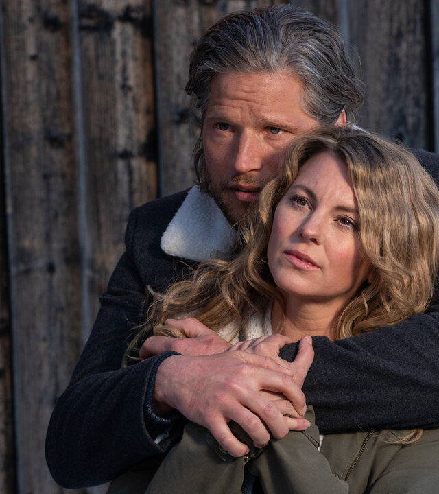 "Die Bergretter: Dieses eine Leben": Vor einem Holztor steht Markus (Sebastian Ströbel) und hat die Arme um Katharina (Luise Bähr) gelegt, die vor ihm steht und nicht unglücklich wirkt.