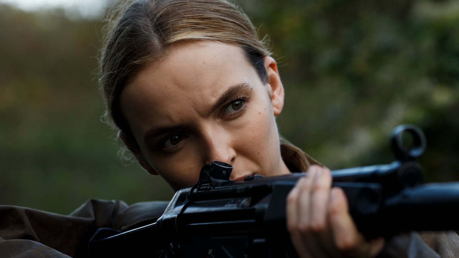 "Killing Eve - Sorry, Baby": Villanelle (Jodie Comer) steht im Wald und zielt konzentriert mit einer Maschinenpistole in die Ferne.