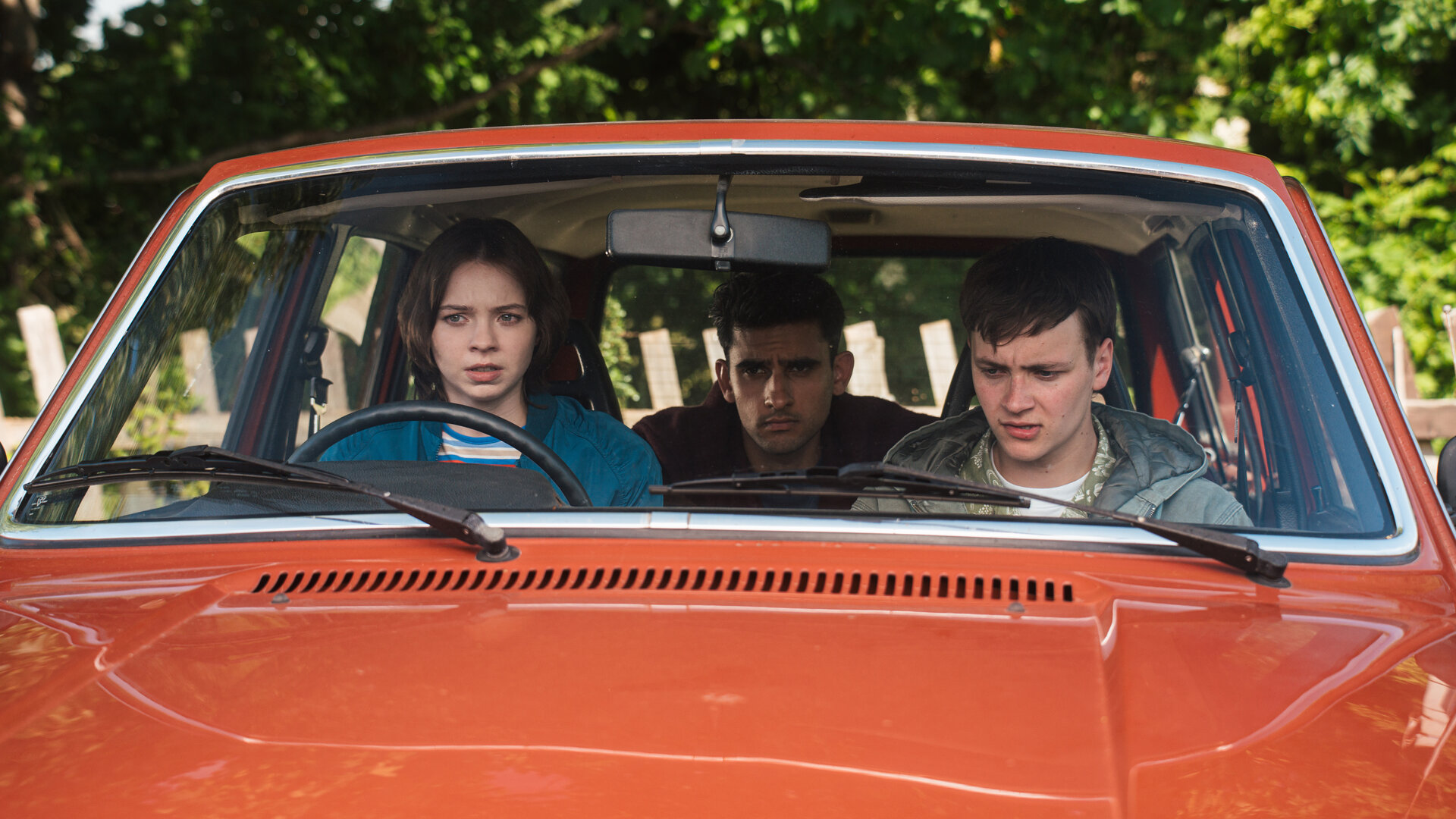"A Good Girl’s Guide to Murder – Wie man einen Catfish angelt": Pip Fitz-Amobi (Emma Myers) sitzt am Steuer eines roten Autos, neben ihr sitzt Connor Reynolds (Jude Morgan-Collie), auf dem Rücksitz Ravi Singh (Zain Iqbal). Alle drei blicken angespannt nach vorn.