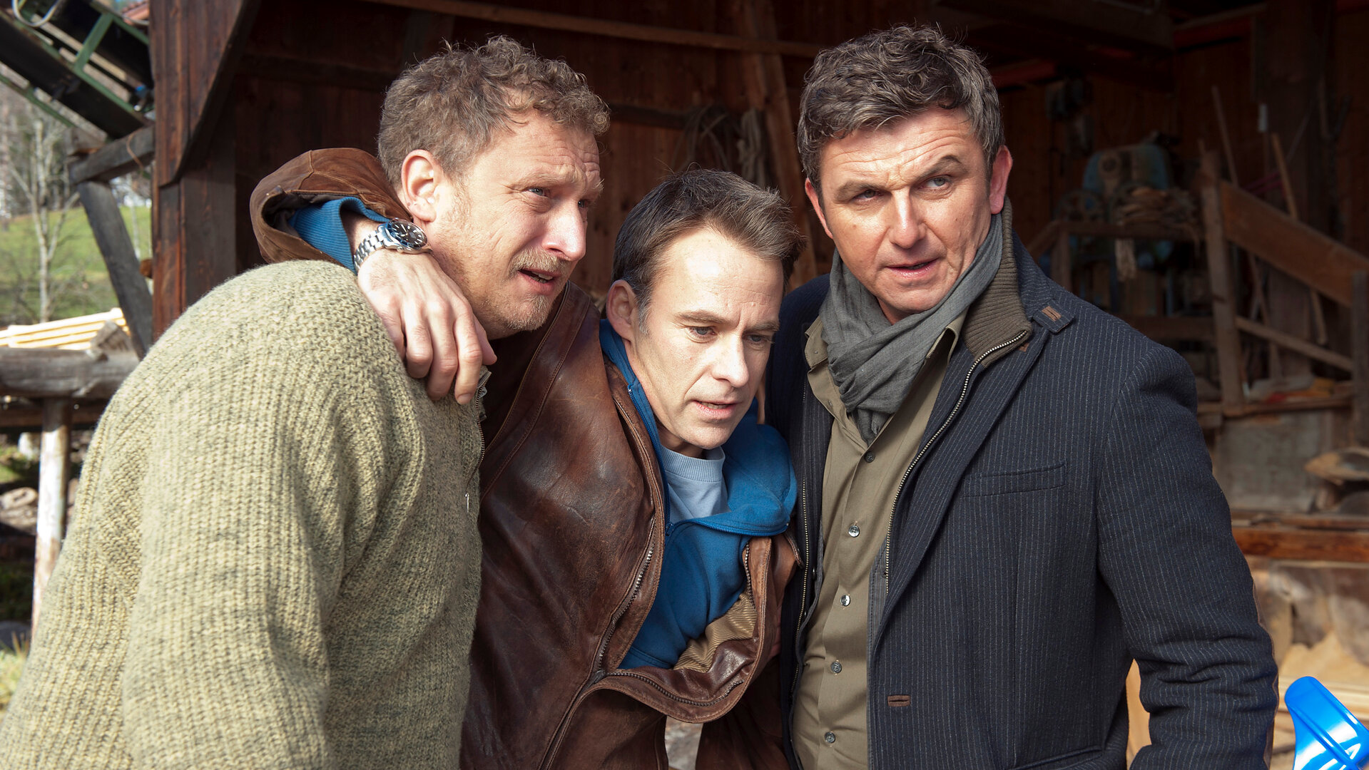 "Der Bergdoktor: Allein (2)": Vor einem Holzhaus: Thomas Weider (Marco Girnth) wird von Roland Angermann (Matthias Komm) und Dr. Martin Gruber (Hans Sigl) gestützt, die jeweils eine seiner  Gehhilfen in der Hand halten.