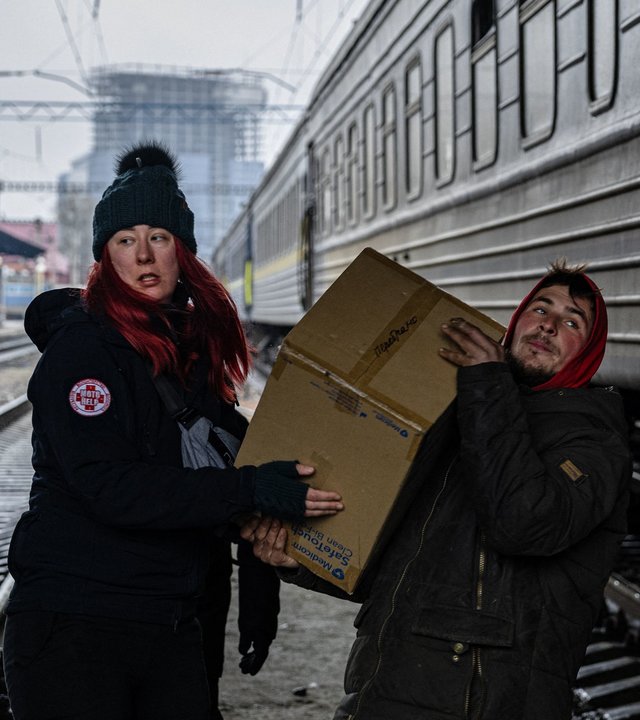 "Tatort Ukraine - Die Freiwilligen": Eine Frau und ein Mann tragen ein schweres Paket in einem menschenleeren Bahnhof über Bahngleis.