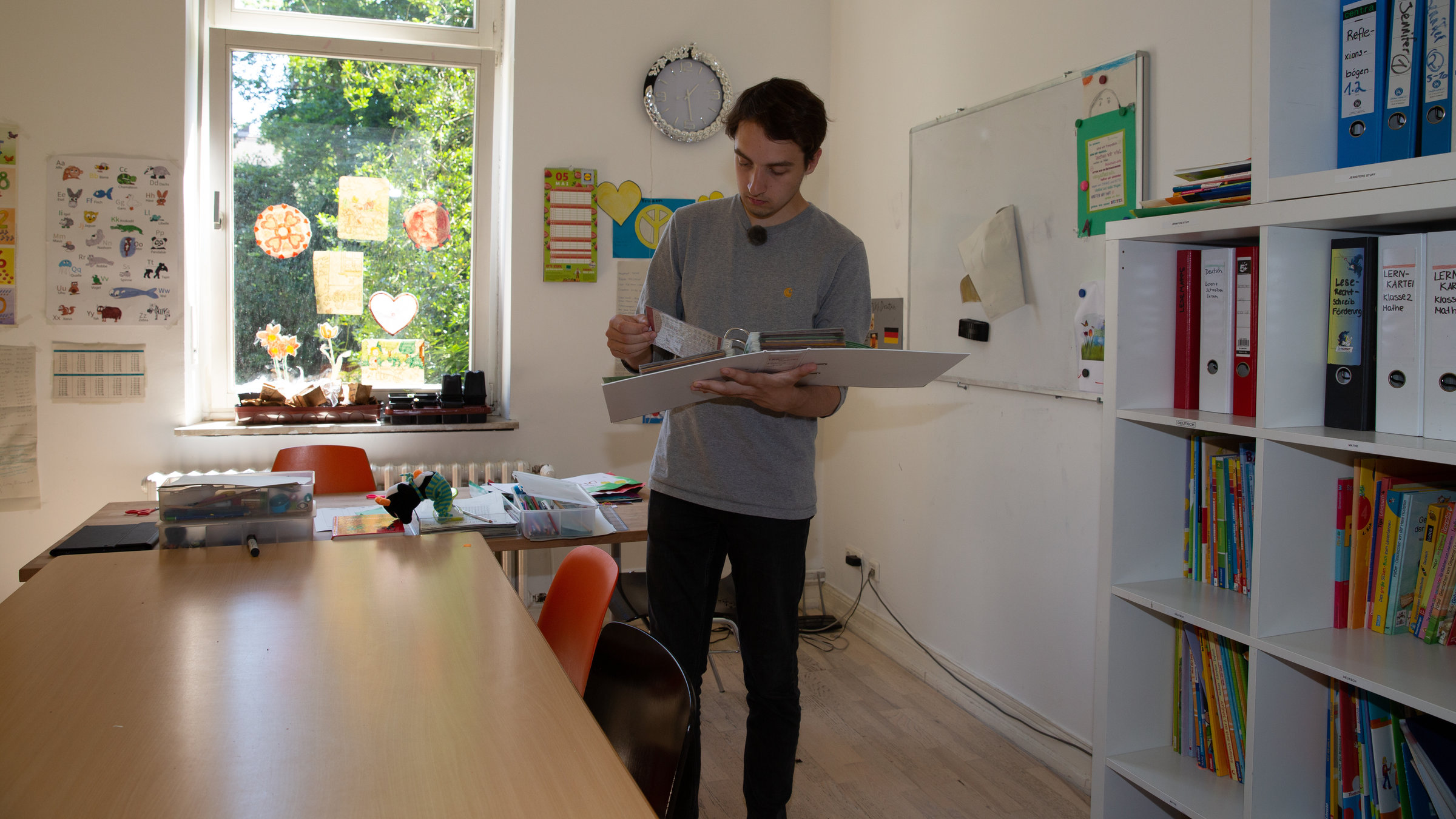 "Einfach Mensch! - Ich engagiere mich!": Tim Hölzel in einem Zimmer mit Buchregalen und einem Holztisch auf der linken Seite.