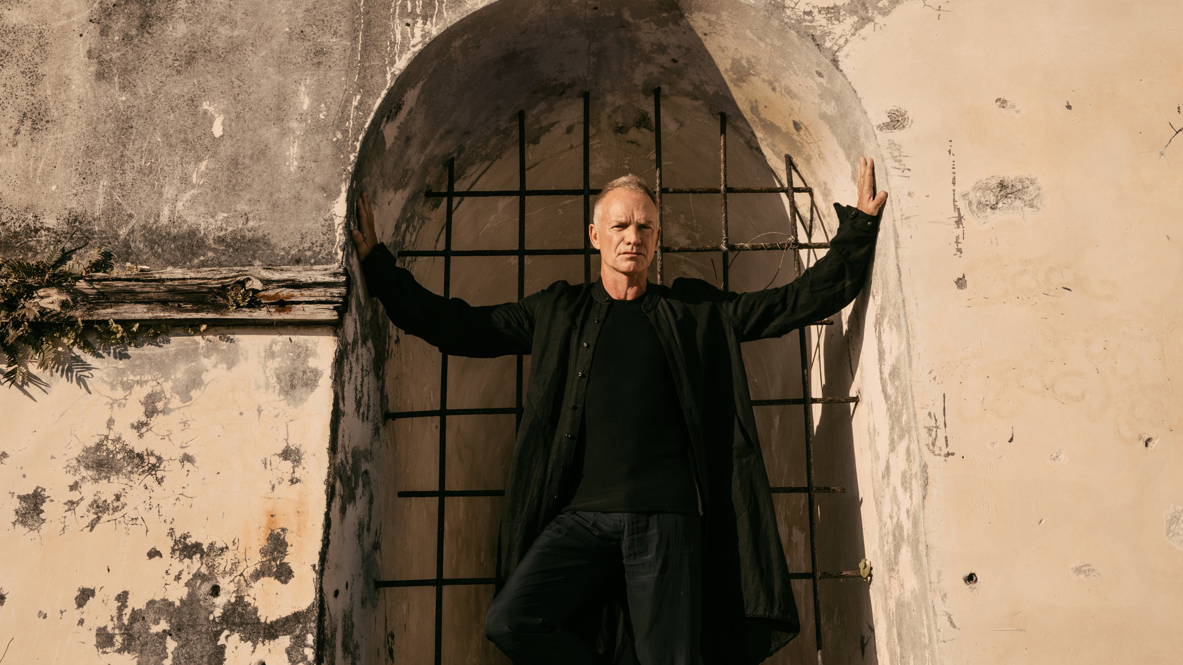 "Sting: My Songs - Live at Château de Chambord":  Der Sänger Sting steht mit ausgebreiteten Armen in einem Torbogen eines alten Gemäuers. Der Eingang hinter ihm ist vergittert. Gekleidet ist er komplett in schwarz.