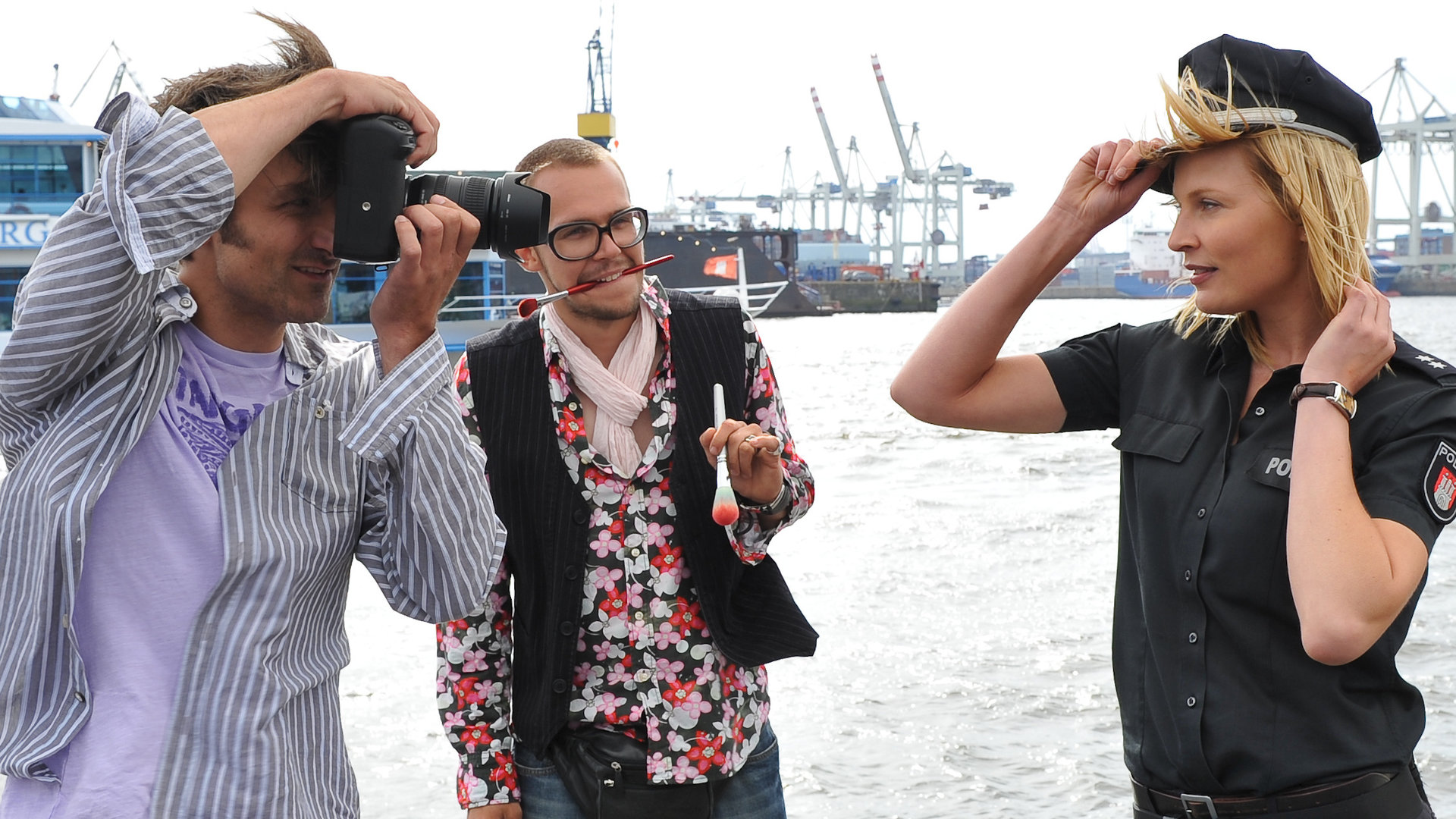 "Notruf Hafenkante - Gefährliche Fotos": Melanie (Sanna Englund) posiert in ihrer Uniform am Hafen. Sie wird von dem Fotografen Lasse (Henning Vogt) abgelichtet. Ein Assistent steht mit Make-up-Pinseln daneben.