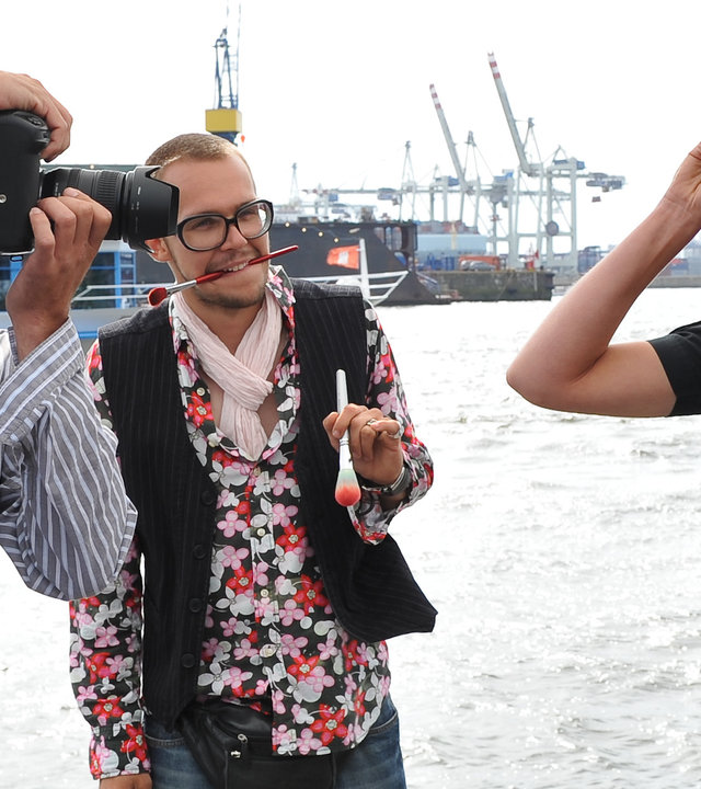 "Notruf Hafenkante - Gefährliche Fotos": Melanie (Sanna Englund) posiert in ihrer Uniform am Hafen. Sie wird von dem Fotografen Lasse (Henning Vogt) abgelichtet. Ein Assistent steht mit Make-up-Pinseln daneben.