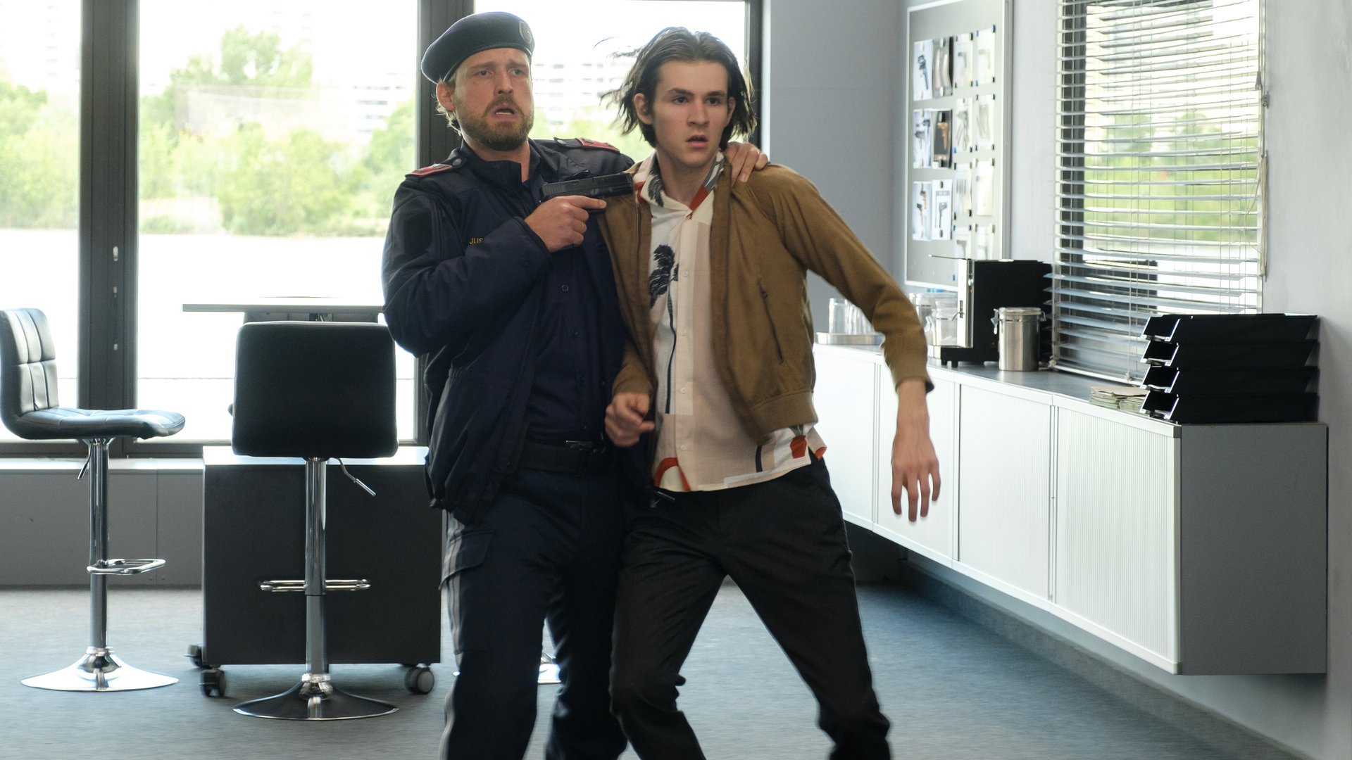 "SOKO Wien - Grenzen": Ludwig Pichler (Fabian Schiffkorn) hat Gio Egger (Enzo Gaier) im Kommissariat an der Schulter gepackt und hält ihm eine Waffe an den Hals.