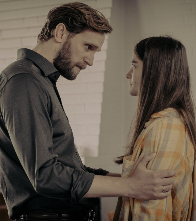 "Another Monday - Grenzen": Malte (Ulrich Brandhoff) und Charlie (Emilie Neumeister) stehen sich gegenüber und reden. Malte hält Charlie an den Armen fest. Im Hintergrund sind ein Kamin und ein Bild an der Wand zu sehen.