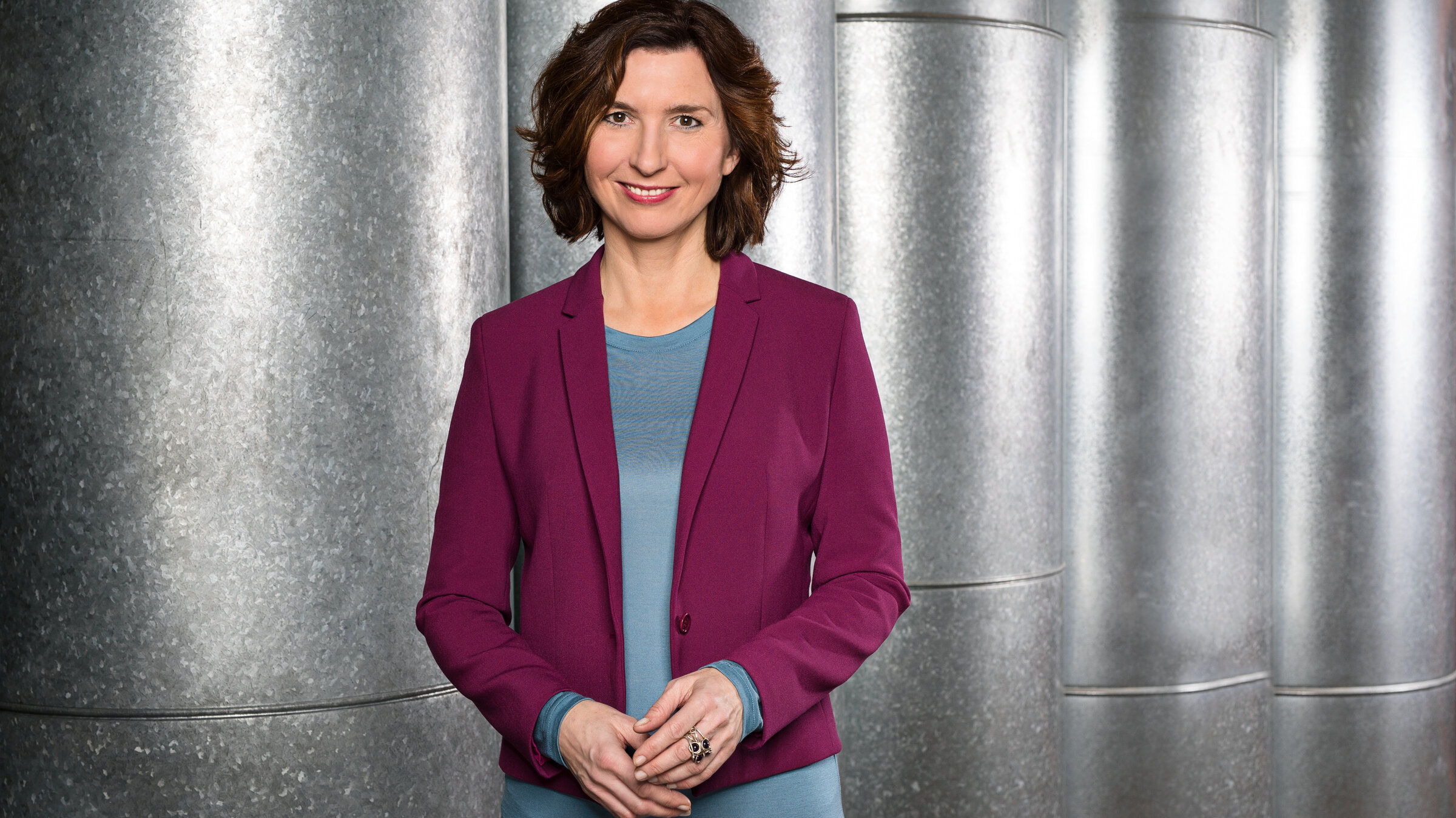 "dein buch - Das Beste von der Leipziger Buchmesse 2025": Porträt von Cécile Schortmann (nur Oberkörper). Sie trägt ein graues Shirt unter einer lilafarbenen Jacke. Sie lächelt in die Kamera.