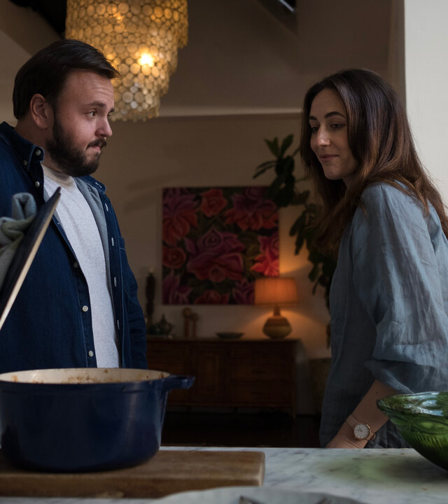 "North Shore – Tod in Sydney – Die Spur des Blutes": Max (John Bradley) und Tori (Claire Lovering) stehen nebeneinander in einem Raum. Vor ihnen ist eine Küchenarbeitsplatte. Max hebt den Deckel eines Kochtopfs an und zeigt Tori den Inhalt.