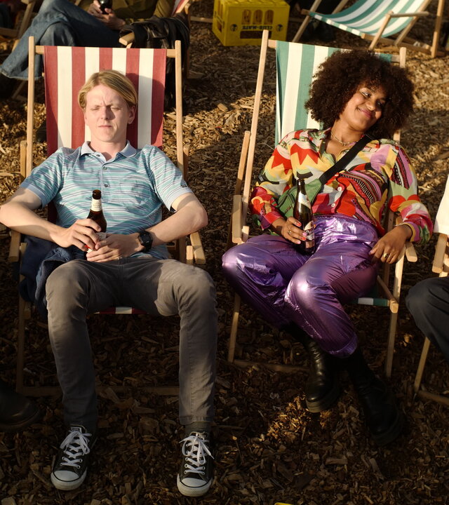 "This Is Gonna Be Great - Erfolg": Hanna (Mona Vojacek Koper), Rob (Jonas Strand Gravli), Aisha (Abigail Abraham) und David (Rein Mulder) sitzen nebeneinander in Liegestühlen. Alle haben Getränkeflaschen in der Hand, David hält zudem noch eine große Tüte Popcorn auf dem Schoß.