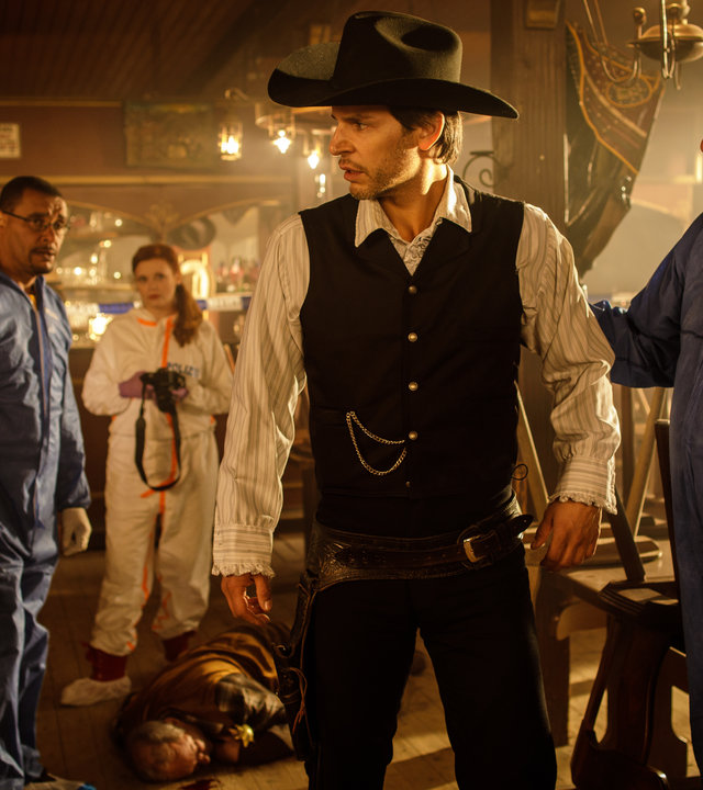 "SOKO München - Himmel Herrgott, Sacramento": In einem Saloon stehen Katharina Hahn (Bianca Hein), Franz Ainfachnur (Christofer v. Beau) und Billie Curio (Sina Reiß). Sie schauen zu Dr. Weissenböck (Florian Odendahl), der als Cowboy verkleidet ist. Hinter ihm steht Arthur Bauer (Gerd Silberbauer) und legt ihm die Hand auf den Rücken. Auf dem Boden liegt eine Leiche.