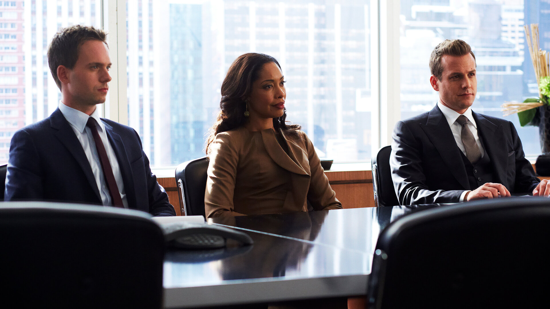 "Suits - Alte Feinde": Mike (Patrick J. Adams), Jessica (Gina Torres) und Harvey (Gabriel Macht) sitzen nebeneinander an einem Konferenztisch. Alle drei blicken angespannt in dieselbe Richtung. Hinter ihnen ist die Skyline New Yorks zu sehen.