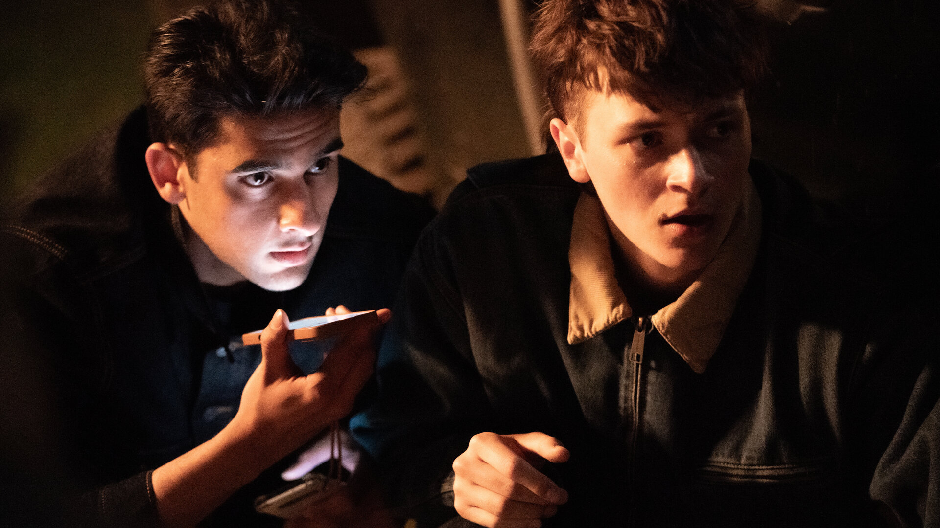"A Good Girl’s Guide to Murder – Der beste doofe Name": Nachts schauen Ravi Singh (Zain Iqbal) und Connor Reynolds (Jude Morgan-Collie) gespannt in eine Richtung. Ravi scheint in ein Smartphone zu sprechen, dass er unter seinem Kinn hält.