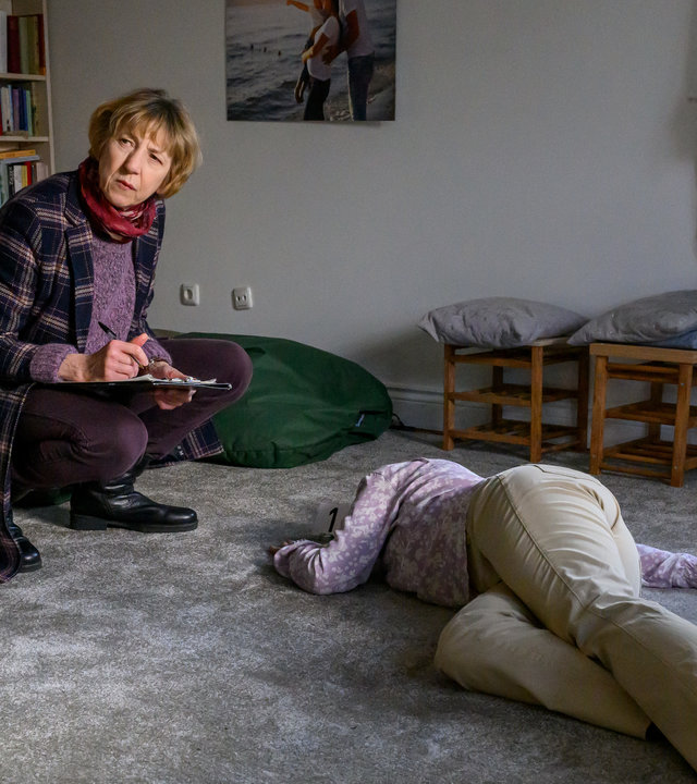 "SOKO Wismar - Tod einer Hebamme": Dr. Helene Sturbeck (Katharina Blaschke) kniet vor der Toten, Anna Stade (Coco Carjell). Dr. Helene Sturbeck hat ein Klemmbrett in der Hand und macht sich Notizen.