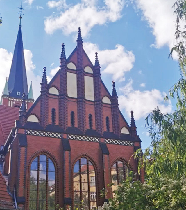 "Evangelischer Gottesdienst - Alles beginnt mit der Sehnsucht": Außenaufnahme der evangelischen Samariterkirche in Berlin-Friedrichshain. Rötlicher Backstein und eine spitz noch oben laufende Bauweise zeichnen sie aus. Die Sonne scheint.