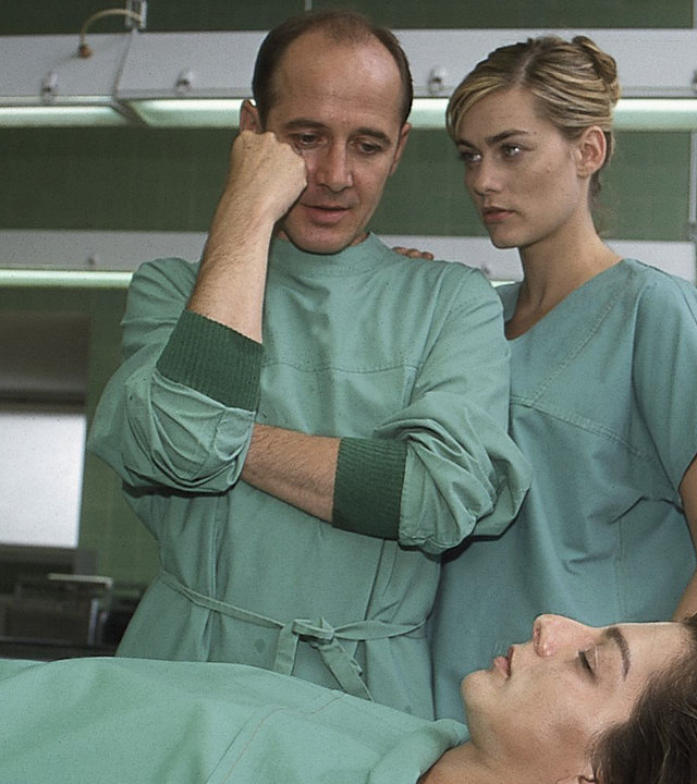 "Der letzte Zeuge - Tod eines Stars": Dr. Robert Kolmaar (Ulrich Mühe) steht im Obduktionssaal vor der Leiche von Sängerin Carla Rauter (Vasiliki Roussi). Er sieht nachdenklich aus.