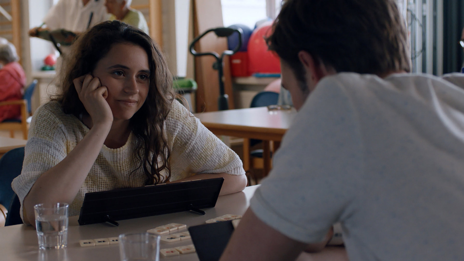 "Sense of Tumour - Tsunami": Tristan (Maarten Nulens) und Hanne (Marthe Schneider) sitzen sich in einem Aufenthaltsraum gegenüber und spielen etwas. Dabei schaut Hanne Tristan aufmerksam an.