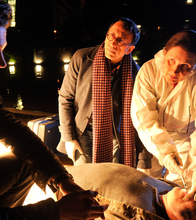 "SOKO Stuttgart - Das Leben des Brian": Jo Stoll (Peter Ketnath), Jan Arnaud (Mike Zaka Sommerfeldt) und Prof. Lisa Wolter (Eva Maria Bayerwaltes) knien bzw. stehen neben dem Opfer Brian Giggs (Komparse, liegend). Es ist Nacht und im Wasser des Neckar spiegeln sich Lichter.