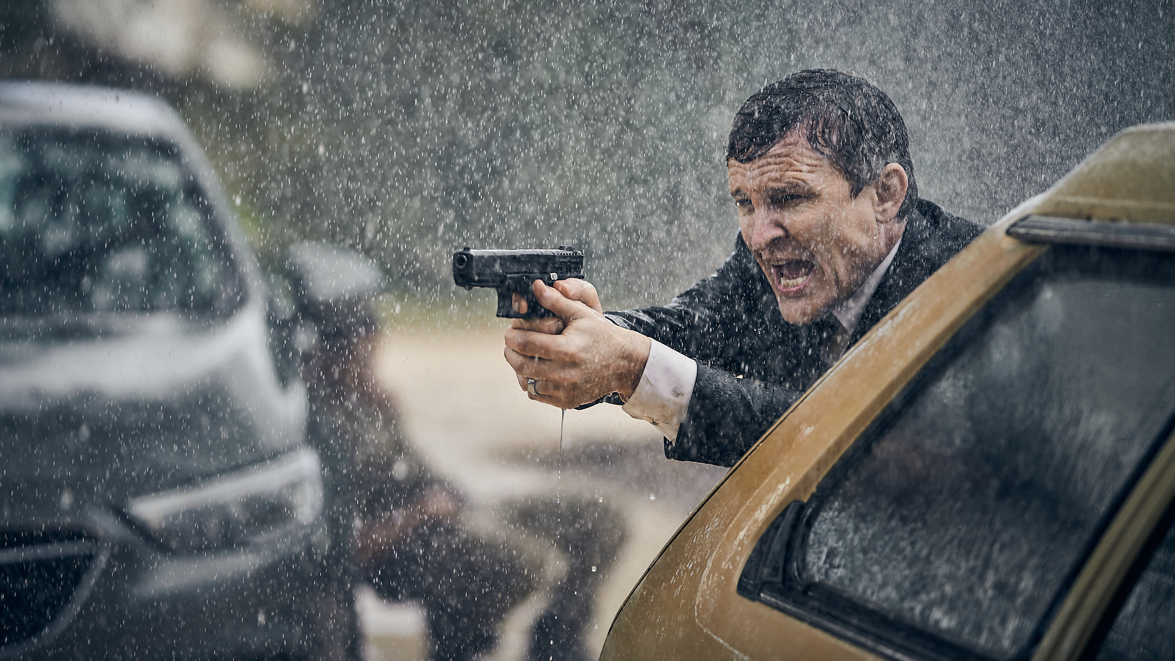 "The Tourist: Hüte dich vor dem Zorn des sanftmütigen Mannes": Detective Inspector Lachlan Rogers (Damon Herriman) steht im strömenden Regen mit gezogener Waffe hinter einem Wagen.