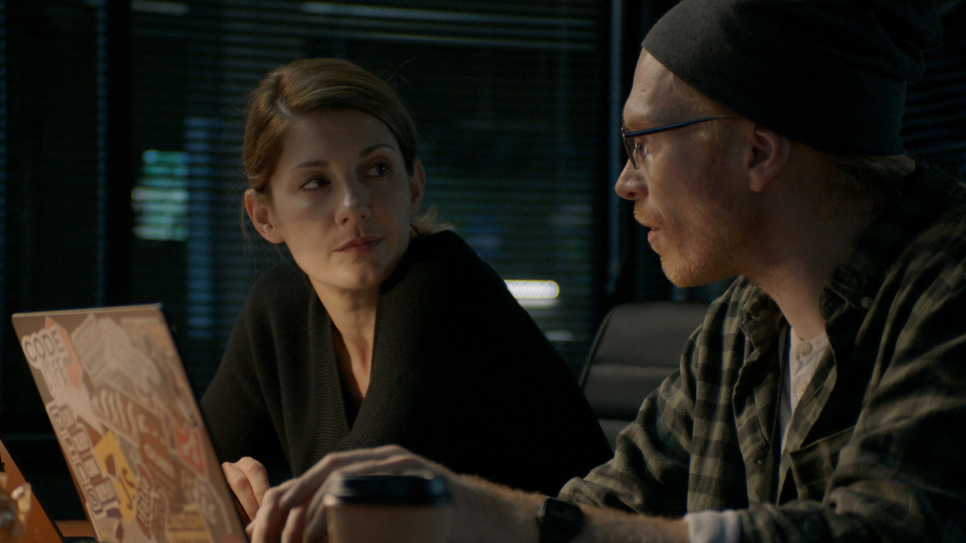 "Hamilton - Undercover in Stockholm (Folge 3)": Kristin Ek (Nina Zanjani) und Birger Hagman (Jörgen Thorsson) sitzen in einem abgedunkelten Raum nebeneinander vor Laptops und unterhalten sich.