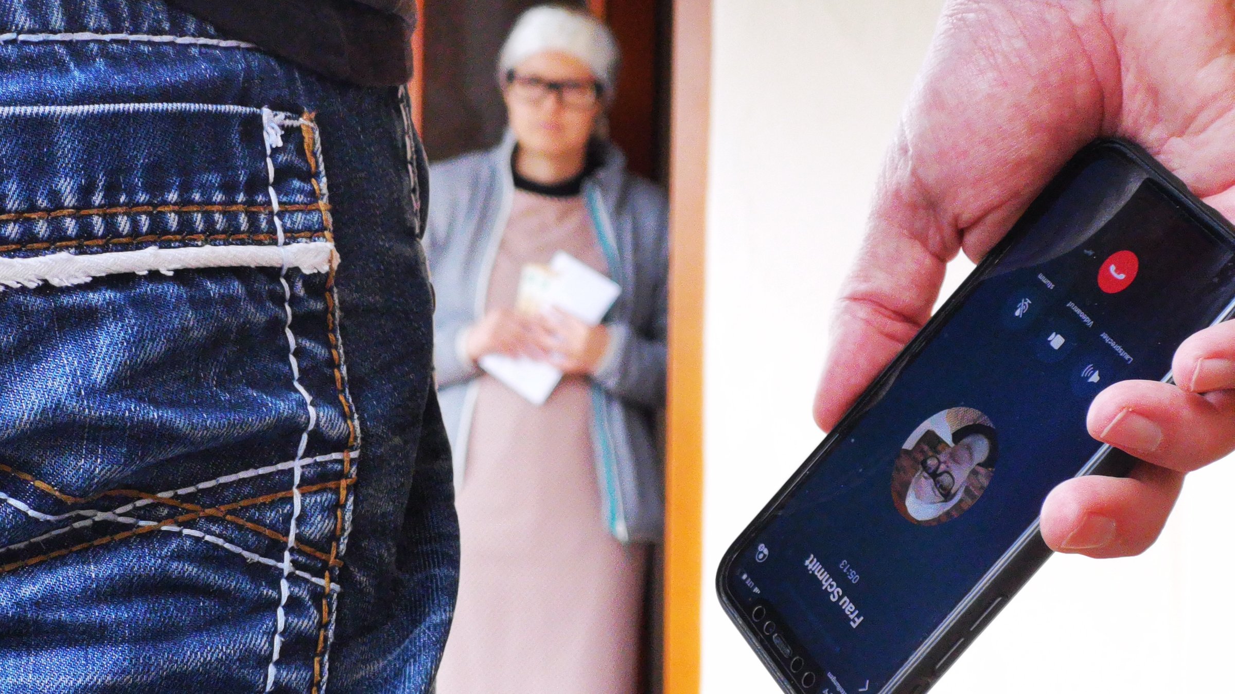 "ZDF.reportage: Vorsicht, Trickdiebe! - Bei Anruf Abzocke!": Symbolbild: Person im Vordergrund  hält ein Smartphone in der Hand. Im Hintergrund ältere weibliche Person in Türeingang.