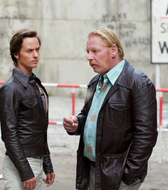 "Der gleiche Himmel (2)": Lars Weber (Tom Schilling) und Ralf Müller (Ben Becker) stehen unweit vom Sperrbezirk und unterhalten sich. Im Hintergrund ist die Berliner Mauer und ein Schild mit der Aufschrift "Achtung! Sie verlassen jetzt West-Berlin" zu sehen.