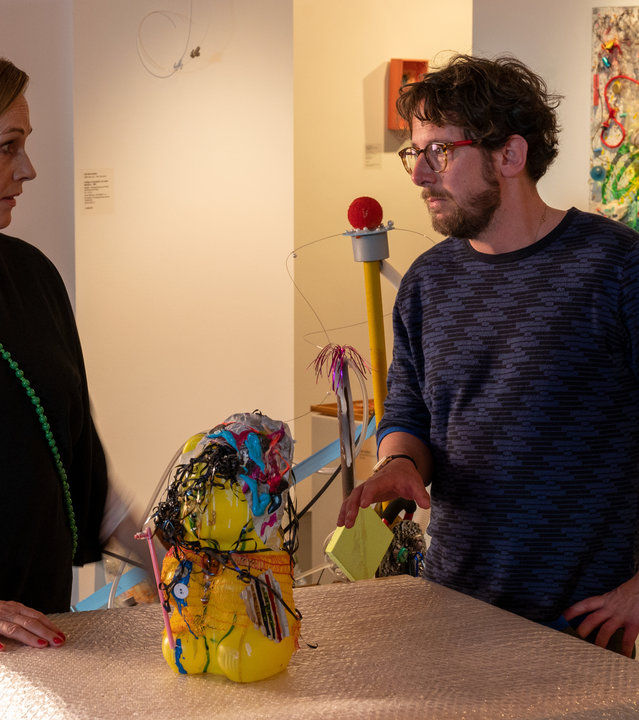 "SOKO Stuttgart - Der gläserne Hund": Vivian Roth (Sabine Bach) steht in der Kunstgalerie an einem Ausstellungstisch. Auf dem Tisch thront eine abstrakte Kunststoffskulptur in leuchtenden Farben. Auf der anderen Seite des Tisches steht Oliver Hagen (Marian Meder). Die beiden schauen sich ernst an.