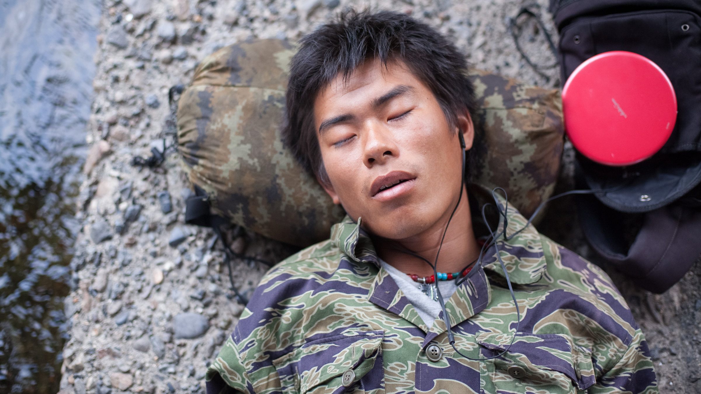 "Ab 18! Freier Mensch": Mit geschlossenen Augen liegt ein junger Mann am Ufer eines Flusses und hört über Kopfhörer Musik.