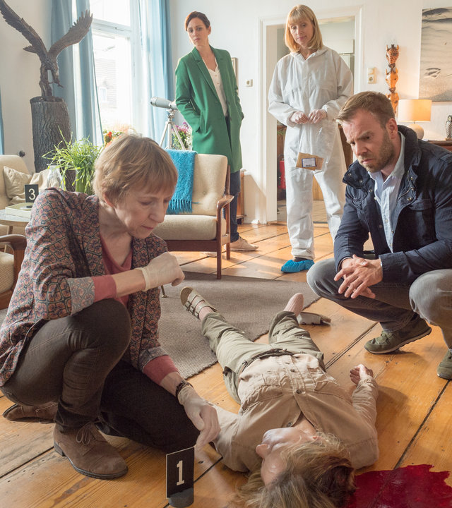 „SOKO Wismar – Herr der Lüfte“: Helene Sturbeck (Katharina Blaschke) kniet neben der toten Silke Rothe (Maria Grau Elias) in deren Wohnzimmer und zeigt ihren Kollegen Lars Pöhlmann (Dominic Boeer), Karoline Joost (Nike Fuhrmann) und Roswitha Prinzler (Silke Matthias) deren tödliche Verletzung.