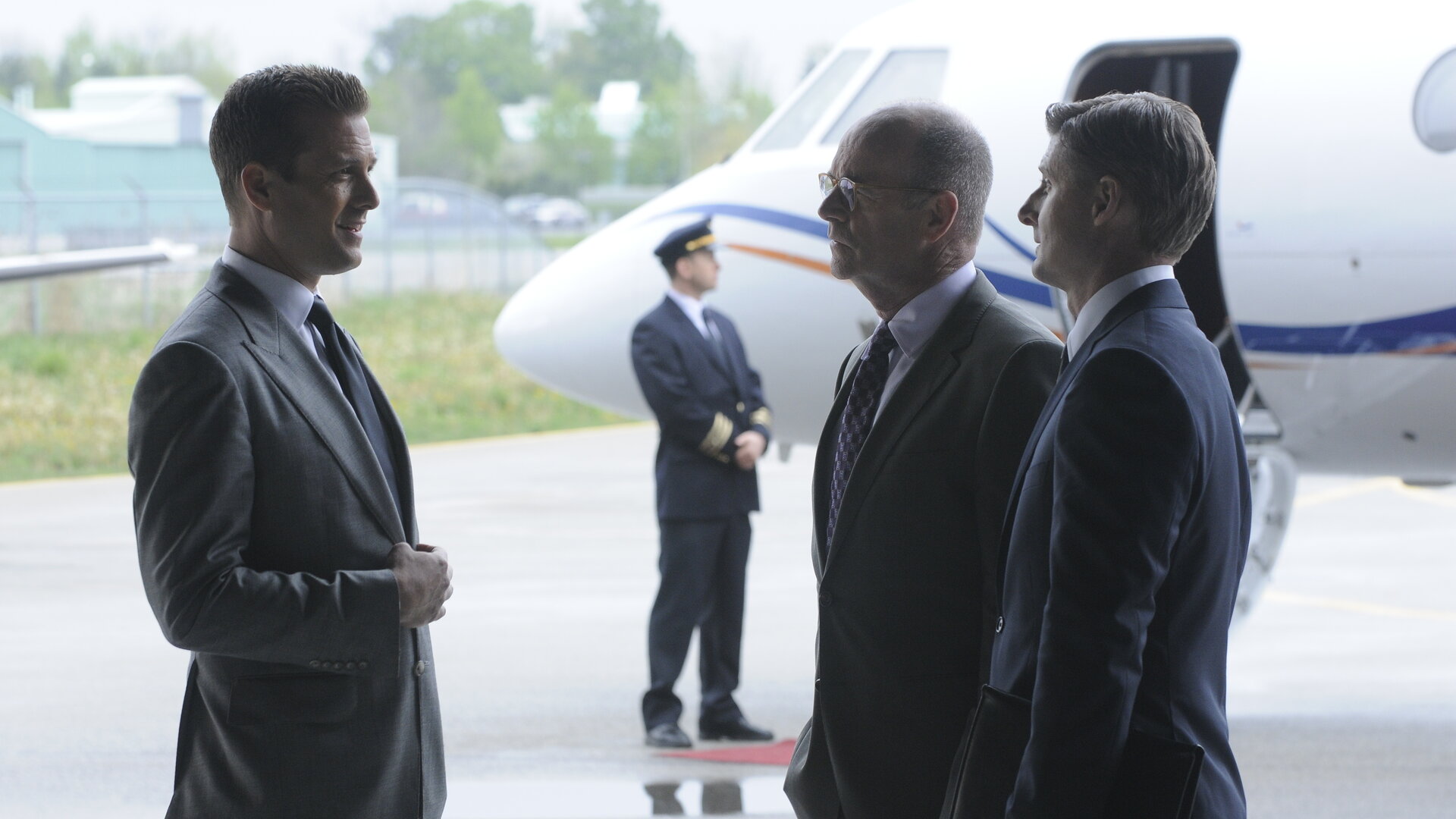 "Suits - Entdeckungen": Harvey (Gabriel Macht) spricht mit Lawrence Kemp (John Finn) und Matt Lasker (Kevin Jubinville), die ihm gegenüberstehen. Im Hintergrund ist ein Privatjet zu sehen, abseits wartet ein Pilot (Komparse) in Uniform.