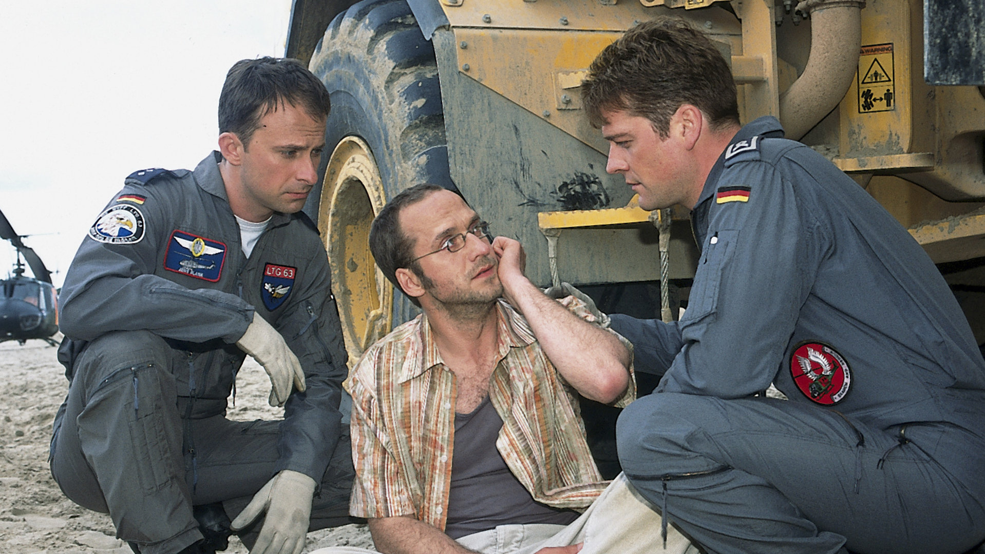 "Die Rettungsflieger - Alte Kameraden": LKW-Fahrer Peter Schneider (Matthias Matz) sitzt verzweifelt auf dem Sandboden einer Baustelle. Rettungsflieger Jens (Nicolas König) und Jan (Oliver Hörner) knien rechts und links neben ihm.