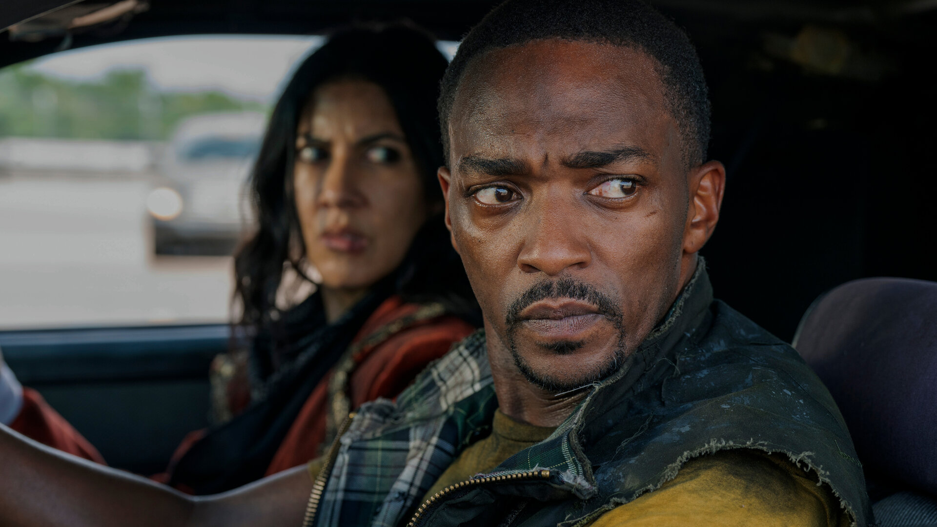 "Twisted Metal - R04DK11": John (Anthony Mackie) sitzt am Steuer eines Fahrzeugs und blickt mit ernster Miene zur Seite. Neben ihm sitzt Quiet (Stephanie Beatriz), die ebenfalls angespannt wirkt und ihn aufmerksam ansieht.