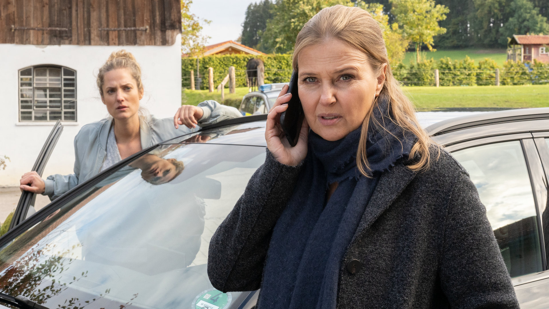 "Die Chefin - Eine Frage der Moral": Vera Lanz (Katharina Böhm) steht vor dem Polizeiwagen und telefoniert mit Paul Böhmer (Jürgen Tonkel), der gerade in einen Unfall verwickelt wurde. Hinter ihr steht ihre besorgte Kollegin Sonni Hüttner (Marie Burchard) in der geöffneten Autotür.