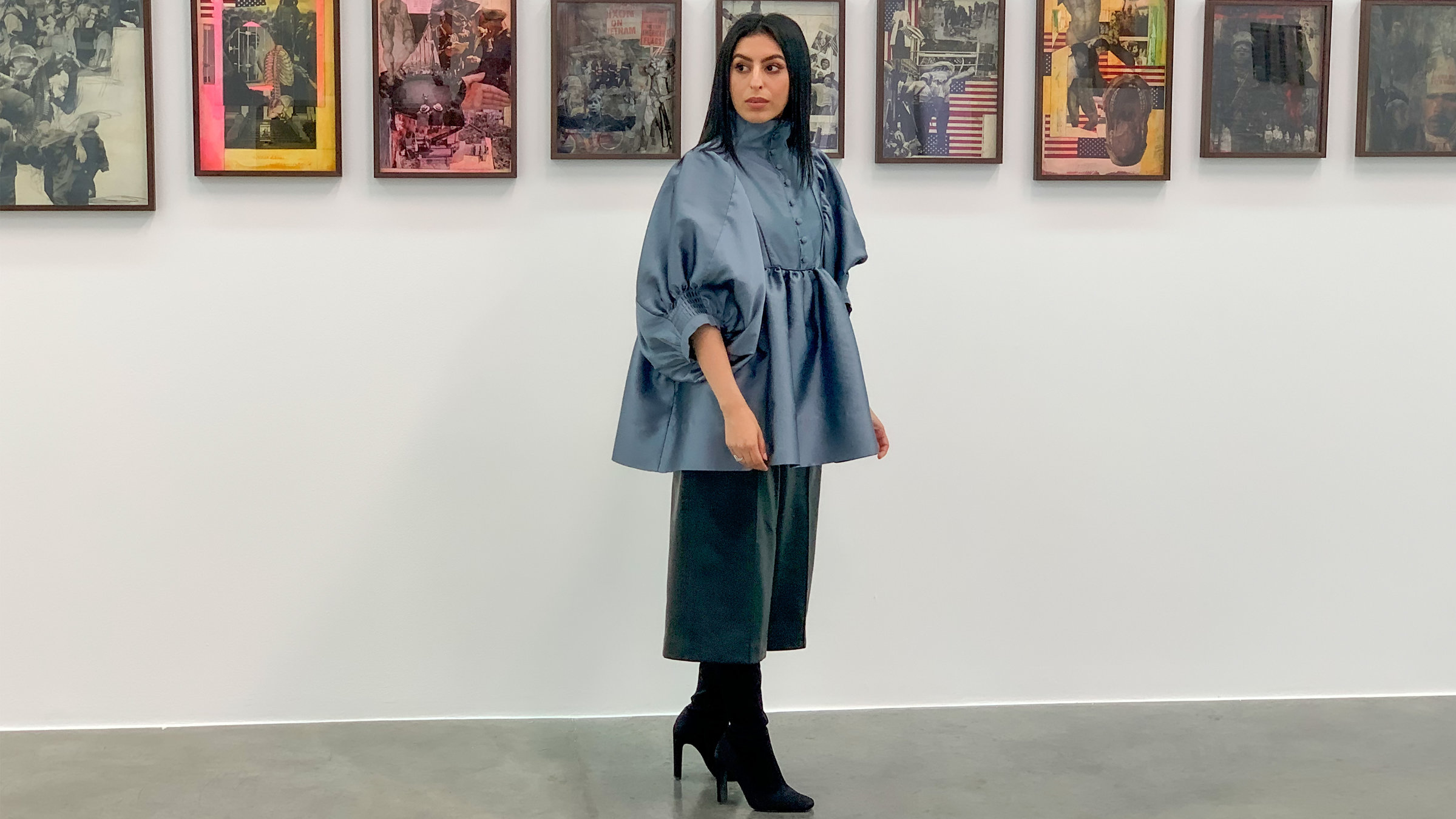 "Muslimisch. Modern. - Frauen auf der arabischen Halbinsel": Eine dunkelhaarige Frau in eleganter Kleidung vor einer Bildergalerie.