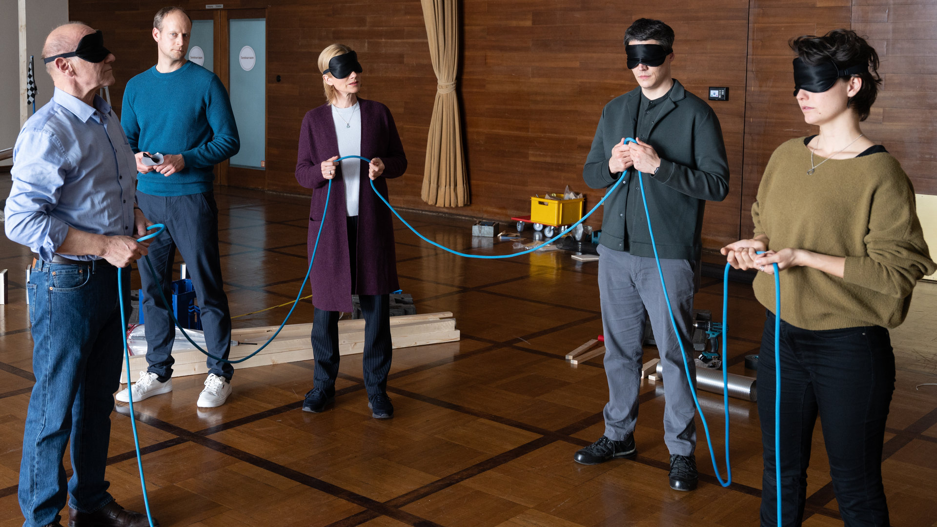 "SOKO Stuttgart - Teams": Michael Kaiser (Karl Kranzkowski), Martina Seiffert (Astrid M. Fünderich), Rico Sander (Benjamin Strecker) und Nele Becker (Nina Siewert) befinden sich in einem großen holzvertäfelten Raum. Sie stehen mit verbundenen Augen im Kreis und halten gemeinsam ein Seil in den Händen. Der Teambuilding-Coach Franz Scherer (Gábor Biedermann) schaut sie erwartungsvoll an. Im Hintergrund sieht man Teile einer noch nicht fertiggestellten Kugelbahn.