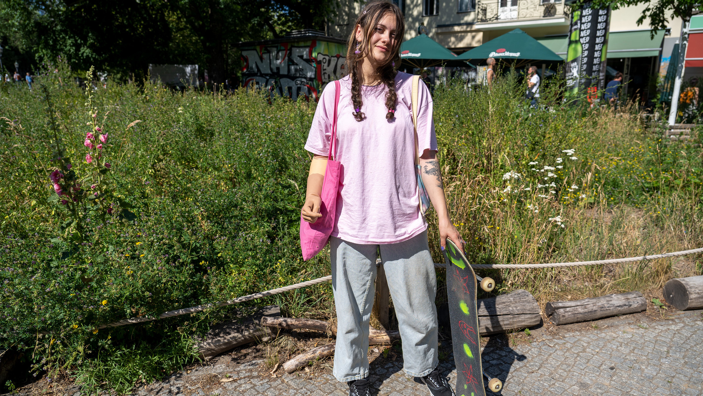 "37°Leben - Schicksalsschlag Amputation": Lina steht vor einem Beet, hält ein Skateboard in der Hand und schaut in die Kamera.