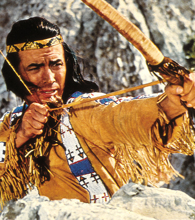 "Winnetou und sein Freund Old Firehand": Großaufnahme von Winnetou (Pierre Brice) mit einem gespannten Bogen vor einer Felslandschaft.